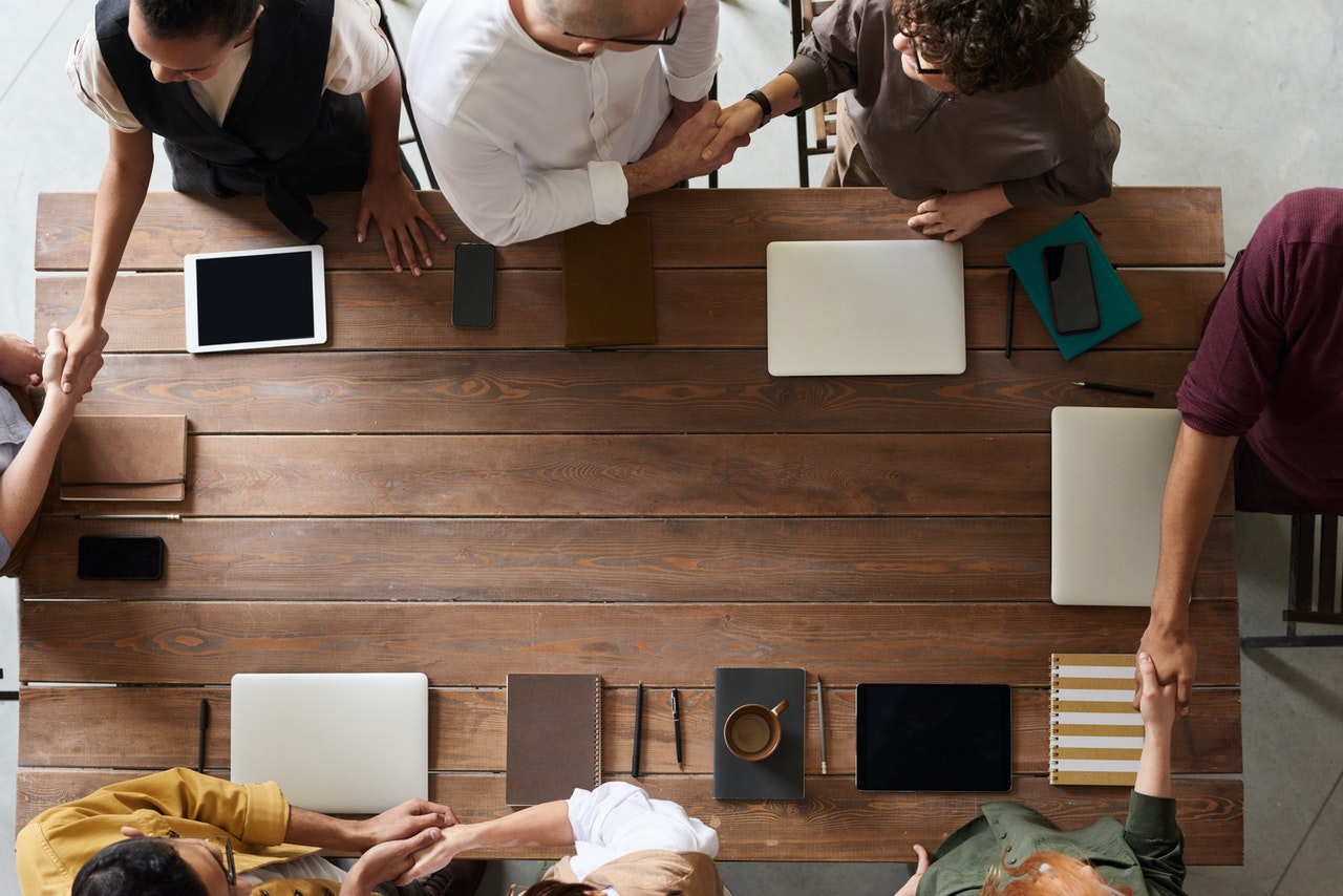 People shaking hands over a table full of tablets, laptops and notebooks, presumably after a meeting